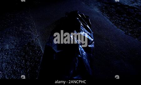 Body bag with corpse lying on wet cold asphalt, victim of murder, crime scene Stock Photo