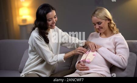 Asian woman putting little socks on her pregnant friend tummy, maternity Stock Photo