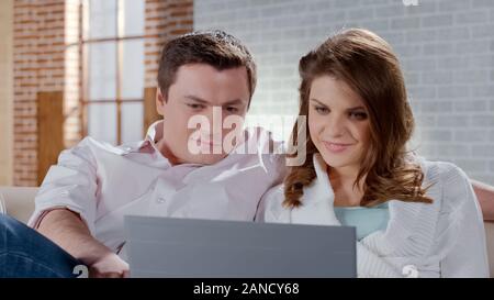 Beautiful wife and husband cuddling on couch, making online orders or purchases Stock Photo