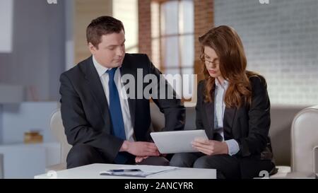 Work colleagues making project on tablet together, discussing business issues Stock Photo