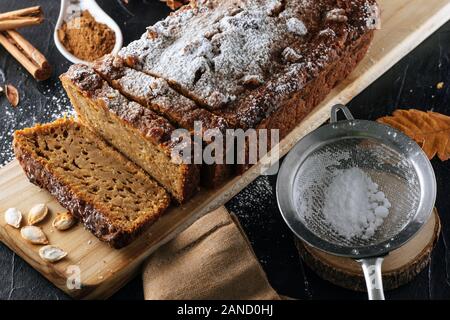 Side view of a pumpkin sponge cake cut into slices with powdered sugar on top, over a wooden board. Still life shot of a fall season image. Stock Photo