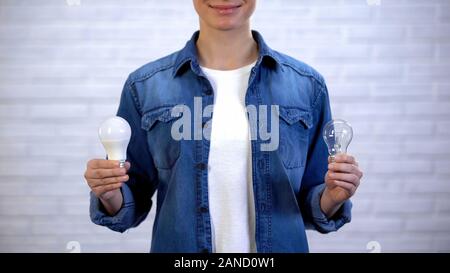 Woman choosing between energy saving led bulb and incandescent lamp, efficiency Stock Photo
