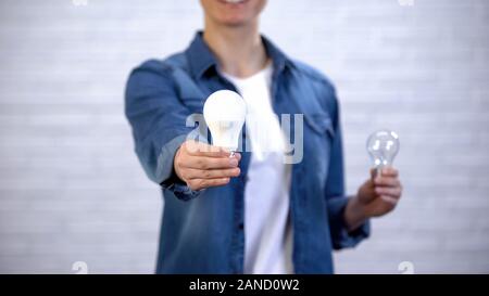 Girl chooses energy saving led bulb instead of incandescent lamp, efficiency Stock Photo