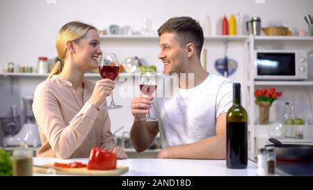 Cheerful couple with wine glasses spending time together at kitchen, romance Stock Photo