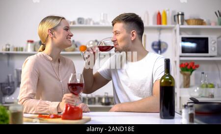 Young couple drinking wine in kitchen, chatting and relaxing together, romance Stock Photo