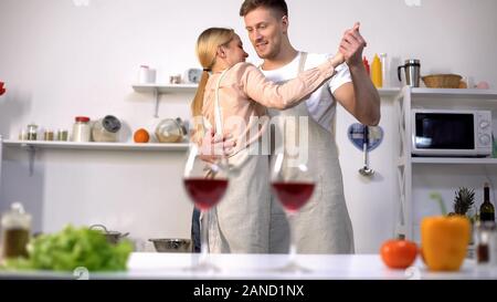 Glasses of red wine on table, romantic couple dancing on background in kitchen Stock Photo