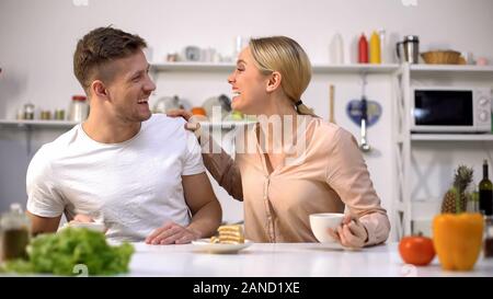 Positive young couple laughing as having breakfast, fooling around together Stock Photo