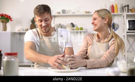 Happy couple clumsily kneading dough, spending fun time together in kitchen Stock Photo