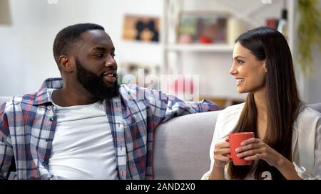 Young mixed-race couple drinking coffee and talking at home, nice conversation Stock Photo