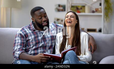 Laughing couple viewing family photo album on sofa, having fun, good memories Stock Photo