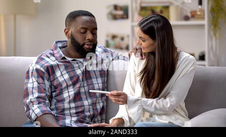 Happy lady showing pregnancy test to Afro-American boyfriend, positive result Stock Photo