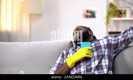 Exhausted black male in gloves lying on sofa, relaxing after house cleaning Stock Photo