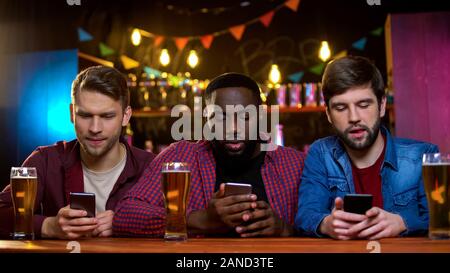 Multiethnic friends using smartphones sitting in pub, problem with communication Stock Photo