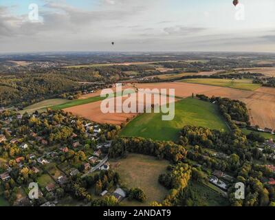 Hot air balloons in the sky over beautiful farmland landscape before sunset time. Colorful hot air balloons flying over the valley during sunset time. Belgium Stock Photo