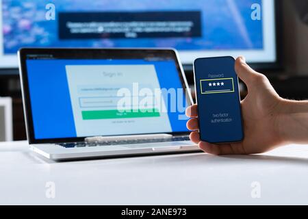 holding a phone and working using laptop, log in on website, double-factor authentication interface Stock Photo