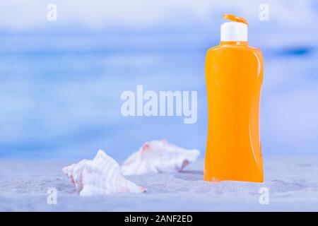Close-up of an orange sunscreen bottle next to two seashells in the sand on an out of focus background. Summer vacation concept. Stock Photo