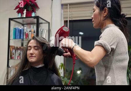 Cromwell, CT / USA - December 27, 2019: Asian hair stylist straightens a female patron's hair Stock Photo