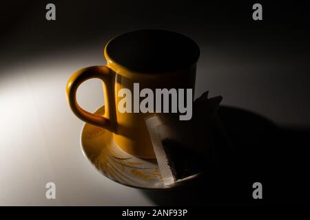 Yellow cup of tea in the shadows, arranged on a plate, with tea bags near the cup. Stock Photo