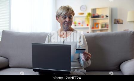 Modern grandma inserting card number on laptop, shopping online, transaction Stock Photo