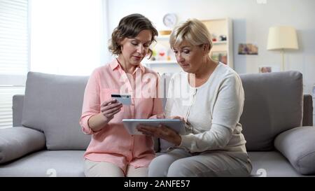 Daughter teaching mature mother using tablet, typing card number, online banking Stock Photo