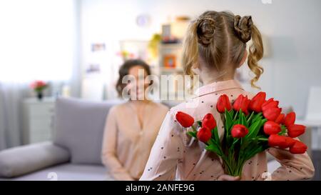 Small child holding present tulips behind back, mothers day congratulations Stock Photo