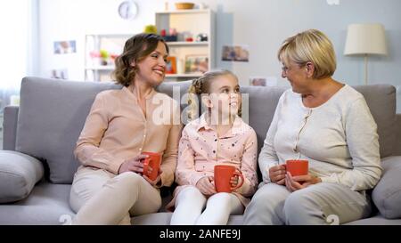 Female family members talking sitting on home sofa with cups of tea, generation Stock Photo