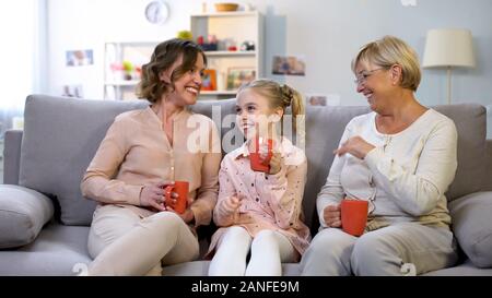 Female family members communicating and laughing, sitting on sofa with cups Stock Photo
