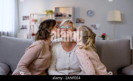 Young female and kid kissing grandmother cheeks, hugging together, family love Stock Photo