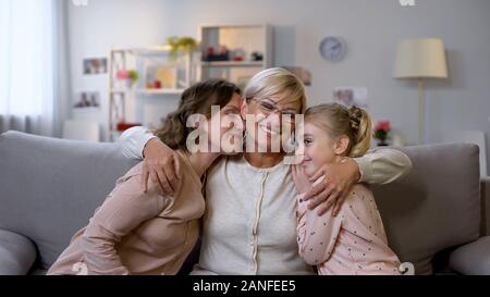 Mother granny and girl hugging, sitting on sofa at home, family closeness, love Stock Photo
