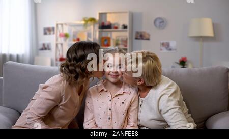 Loving mother and granny kissing daughter cheeks and hugging, female generations Stock Photo