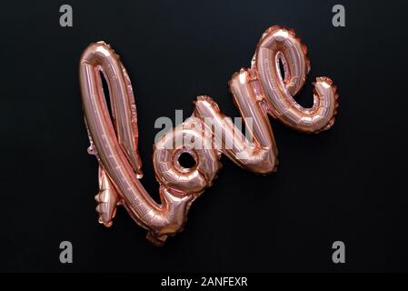 Love word from pink inflatable balloon on black background. The concept of romance, Valentine's Day. Love rose gold foil balloon isolated on black Stock Photo