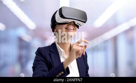 Smiling manager in virtual reality headset scrolling images, office technology Stock Photo