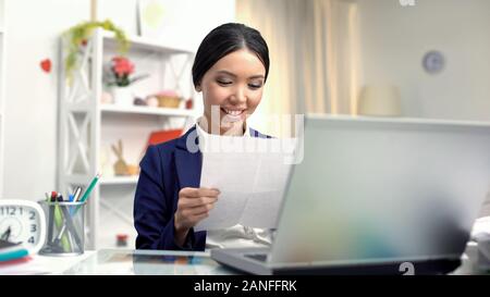 Young smiling female reading letter sitting front of laptop, correspondence Stock Photo