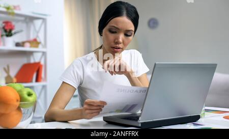 Freelance designer holding document working laptop at home, workload deadline Stock Photo