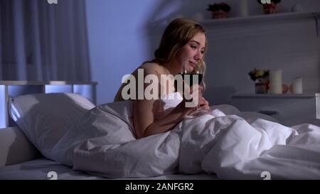 Upset woman with glass of red wine crying in bed, feeling broken heart, divorce Stock Photo