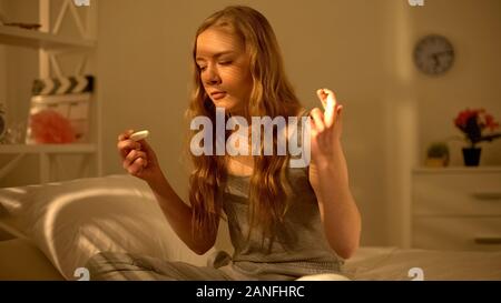 Teen girl looking at pregnancy test in hands waiting for result, birth control Stock Photo