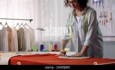 Concentrated tailor cutting workpiece from fabric, woman working on atelier Stock Photo