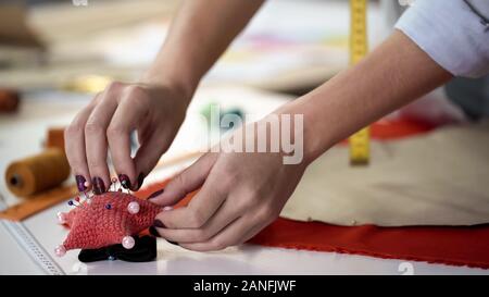 Girl taking pins from needles pad and fixing template on fabric before cutting Stock Photo