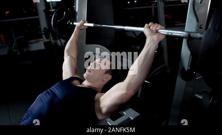 Strong man doing barbell bench press in gym, personal bodybuilding program Stock Photo
