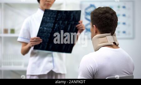 Traumatologist showing neck xray to male in foam cervical collar, bad diagnosis Stock Photo