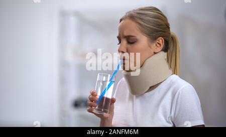 Girl in foam cervical collar trying to drink glass water with straw poor attempt Stock Photo