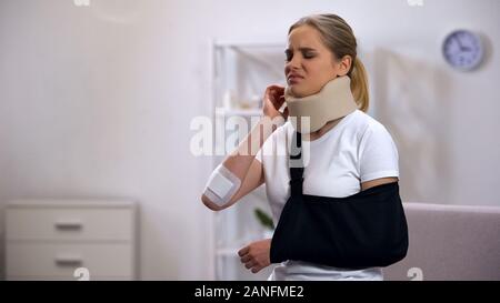 Injured woman in foam cervical collar and arm sling suffering pain in shoulder Stock Photo