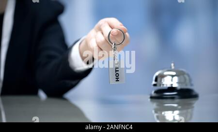 Female hand holding Hotel room keys near bell on reception, hospitality services Stock Photo