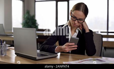 Woman checking social media on phone, distracted from work, productivity concept Stock Photo