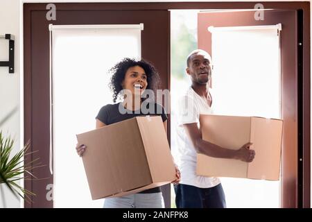 Excited black couple carrying boxes impressed entering new home Stock Photo