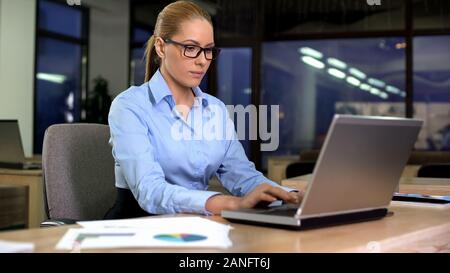 Concentrated manager working on laptop at night shift in office, extra hours Stock Photo