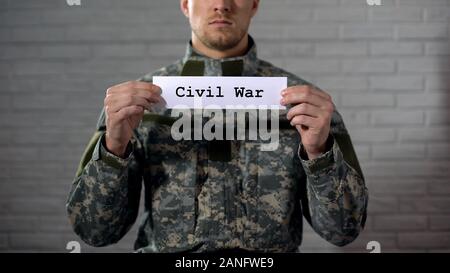 Civil war word written on sign in hands of male soldier, cruelty and death Stock Photo