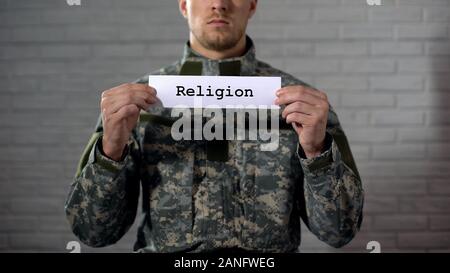 Religion word written on sign in hands of male soldier, faith in God, prayer Stock Photo
