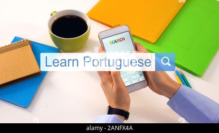 Person typing learn Portuguese phrase on smartphone search bar, education Stock Photo
