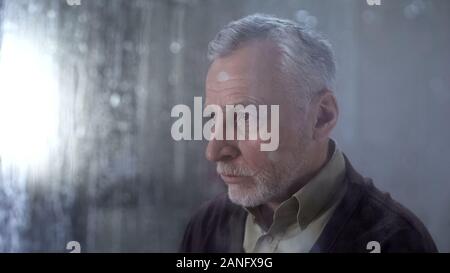 Senior man feeling sad, rain drops on window glass, depression concept, lonely Stock Photo